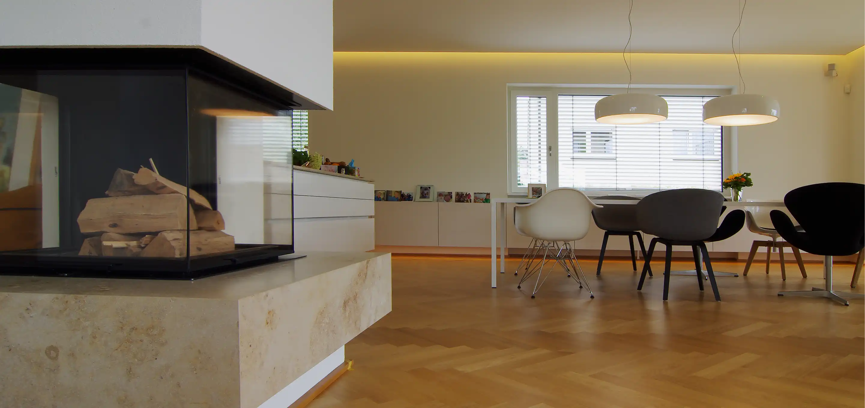 Wohn- und Essbereich mit Kamin, Designerstühlen, weißen Sideboards und indirekter Wandbeleuchtung