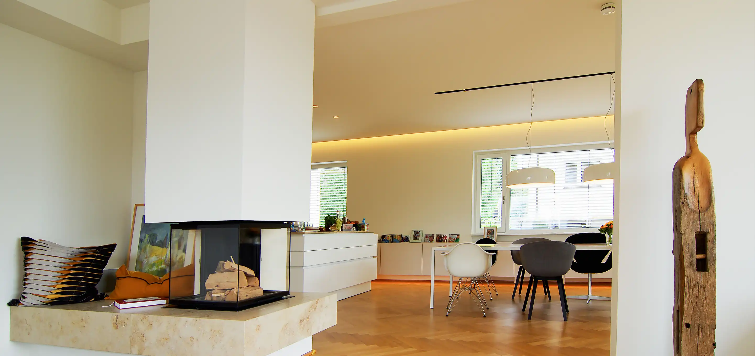 Wohnbereich mit Kamin, Esstisch, Hängeleuchten und weißen Sideboards